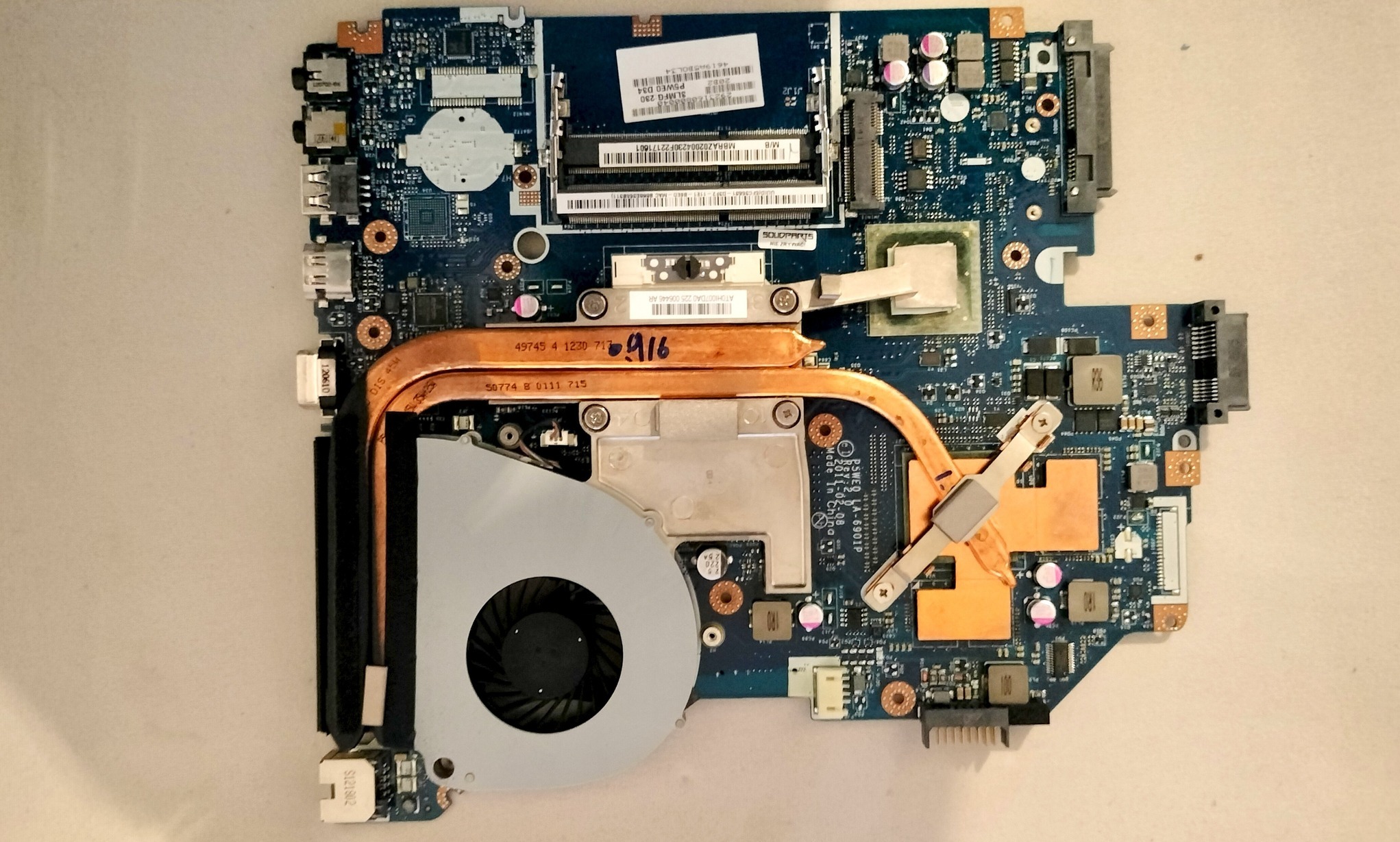 Płyta główna laptopa z widocznym systemem chłodzenia, elementami elektronicznymi i gniazdami. Detaliczne ujęcie z bliska, ukazujące skomplikowaną budowę i komponenty.