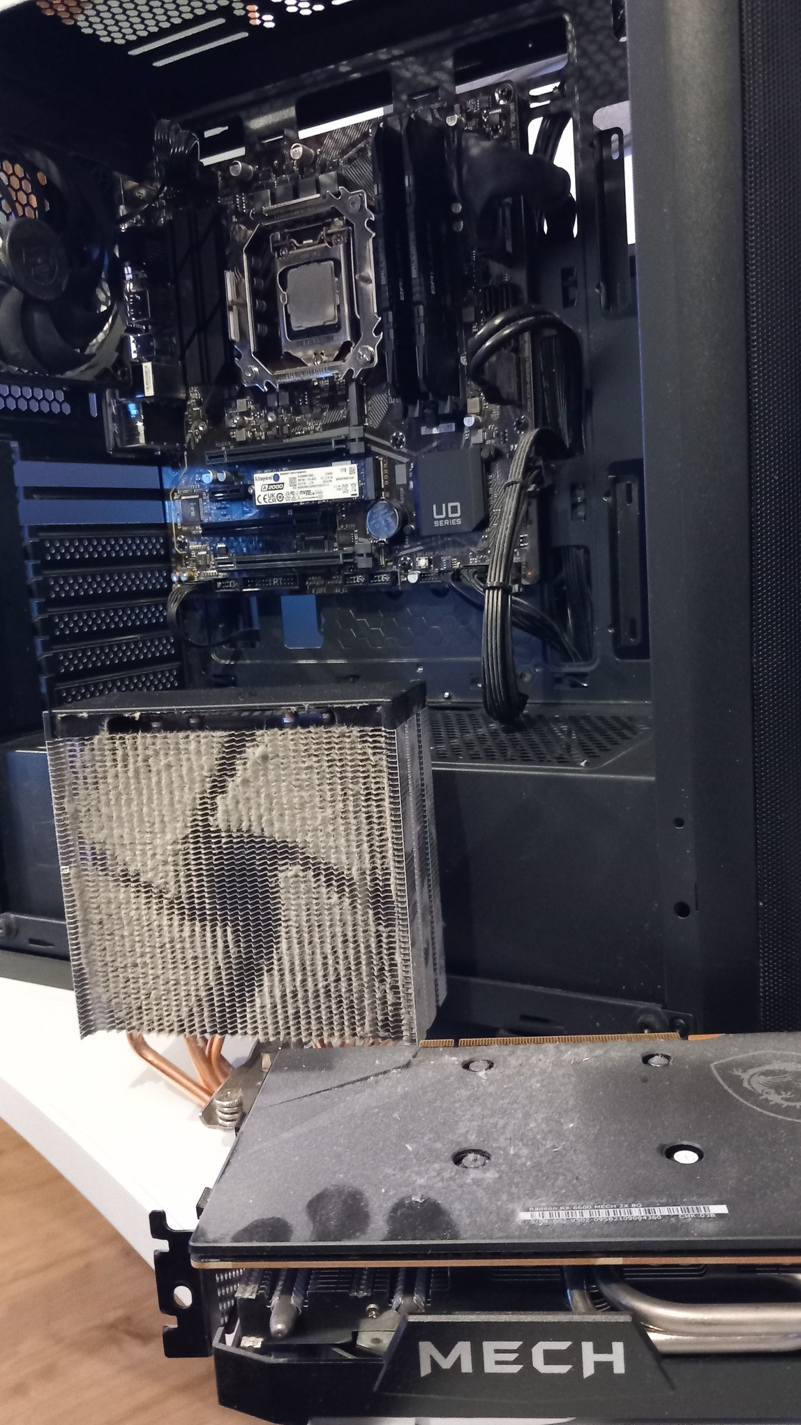 Otwarta obudowa komputera stacjonarnego z zakurzoną kartą graficzną MSI Mech i radiatorem procesora. Widoczna płyta główna i inne komponenty. Wnętrze PC przed czyszczeniem.