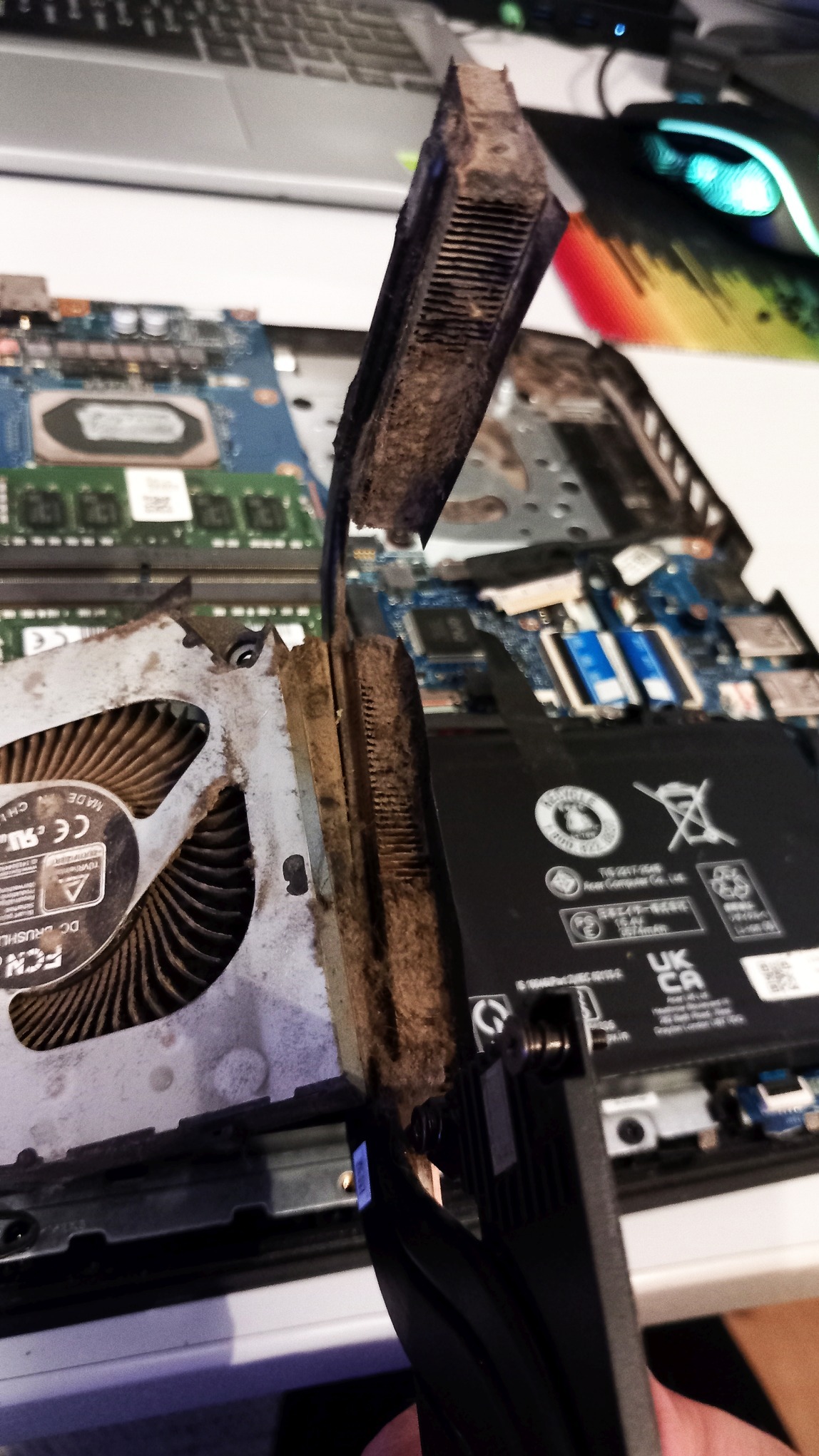 Otwarty laptop z widocznym, zakurzonym układem chłodzenia (wentylator i radiator) podczas czyszczenia. Widoczne elementy płyty głównej i baterii.