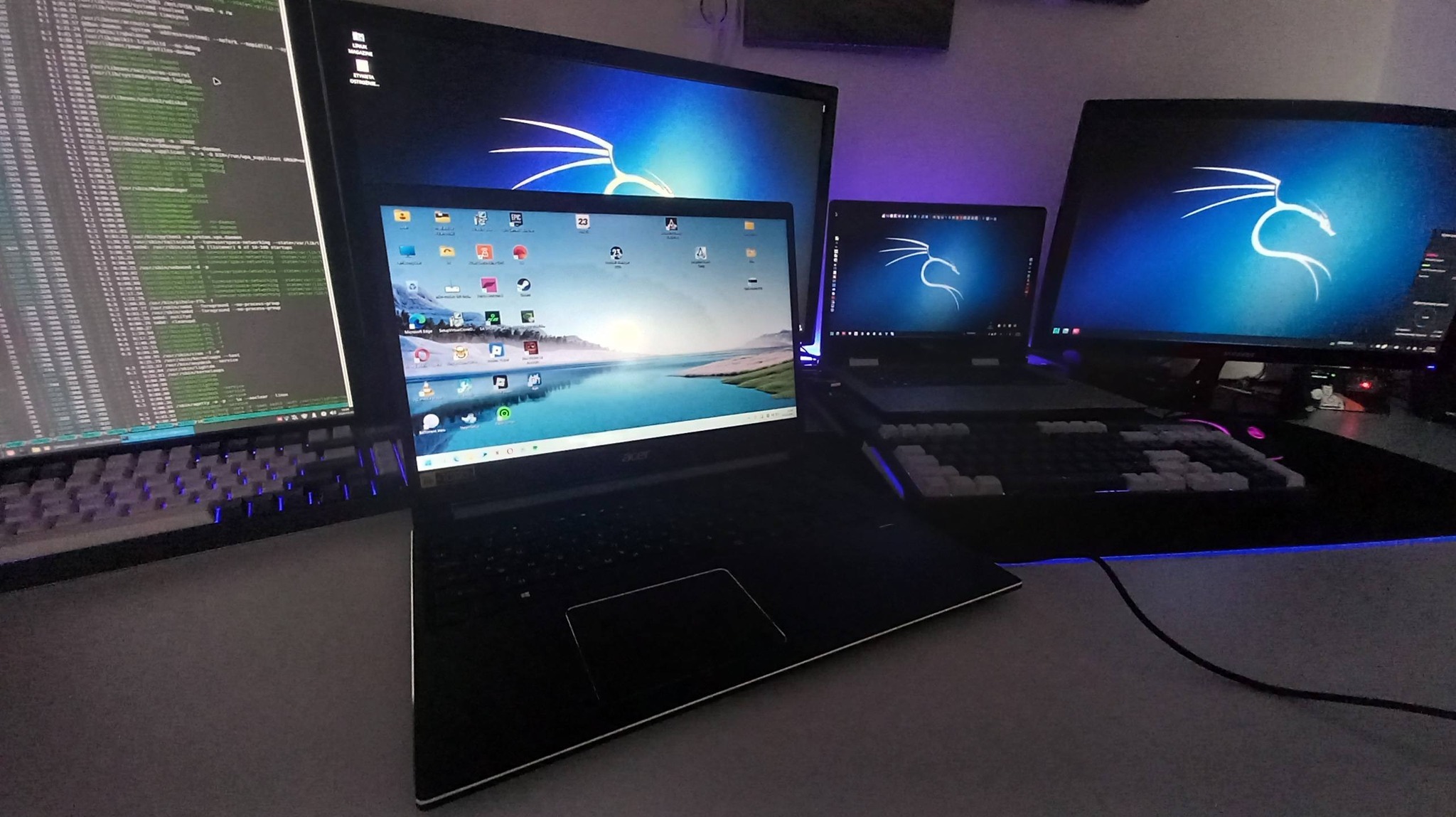 Stanowisko pracy IT w Pyrzycach: kilka monitorów i laptopów z uruchomionym kodem i systemem operacyjnym Kali Linux. Podświetlana klawiatura mechaniczna.