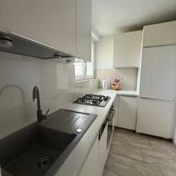 Michał - Jasna kuchnia po remoncie: minimalistyczne białe szafki, szary zlew z baterią, płyta gazowa i drewnopodobne płytki podłogowe. Nowoczesne wykończenie wnętrza.