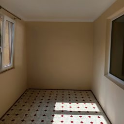 Michał - Pomalowane na beżowo puste pomieszczenie z oknami i wzorzystą podłogą w romby, oświetlone promieniami słońca. Widok na odnowione wnętrze.
