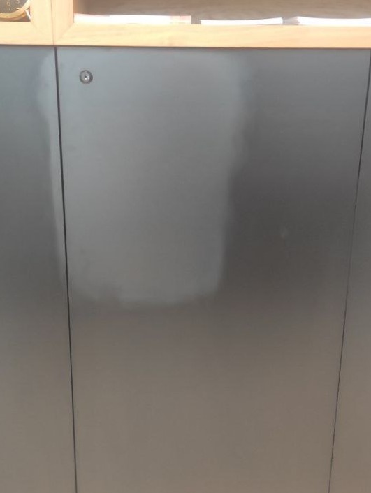 Szara szafka z widocznym obszarem po czyszczeniu, ukazującym odzyskanie naturalnego koloru i odtłuszczenie powierzchni. Detal z bliska, oświetlenie naturalne.