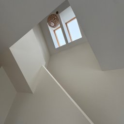 Ivan Shubin - Białe ściany i sufit po malowaniu, widok z dołu na okna dachowe i lampę z wikliny. Geometryczne kształty i minimalistyczny design.