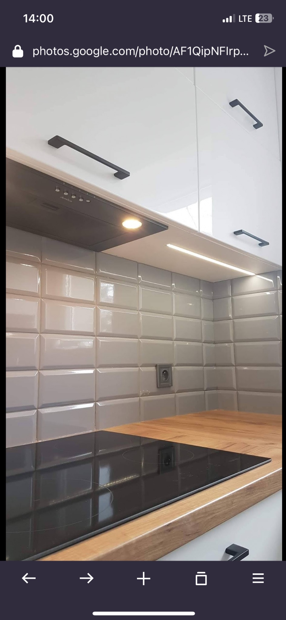 Nowoczesna kuchnia z szarymi, wypukłymi płytkami, drewnianym blatem i czarną płytą indukcyjną. Oświetlenie LED pod szafkami i czarne uchwyty dodają elegancji.