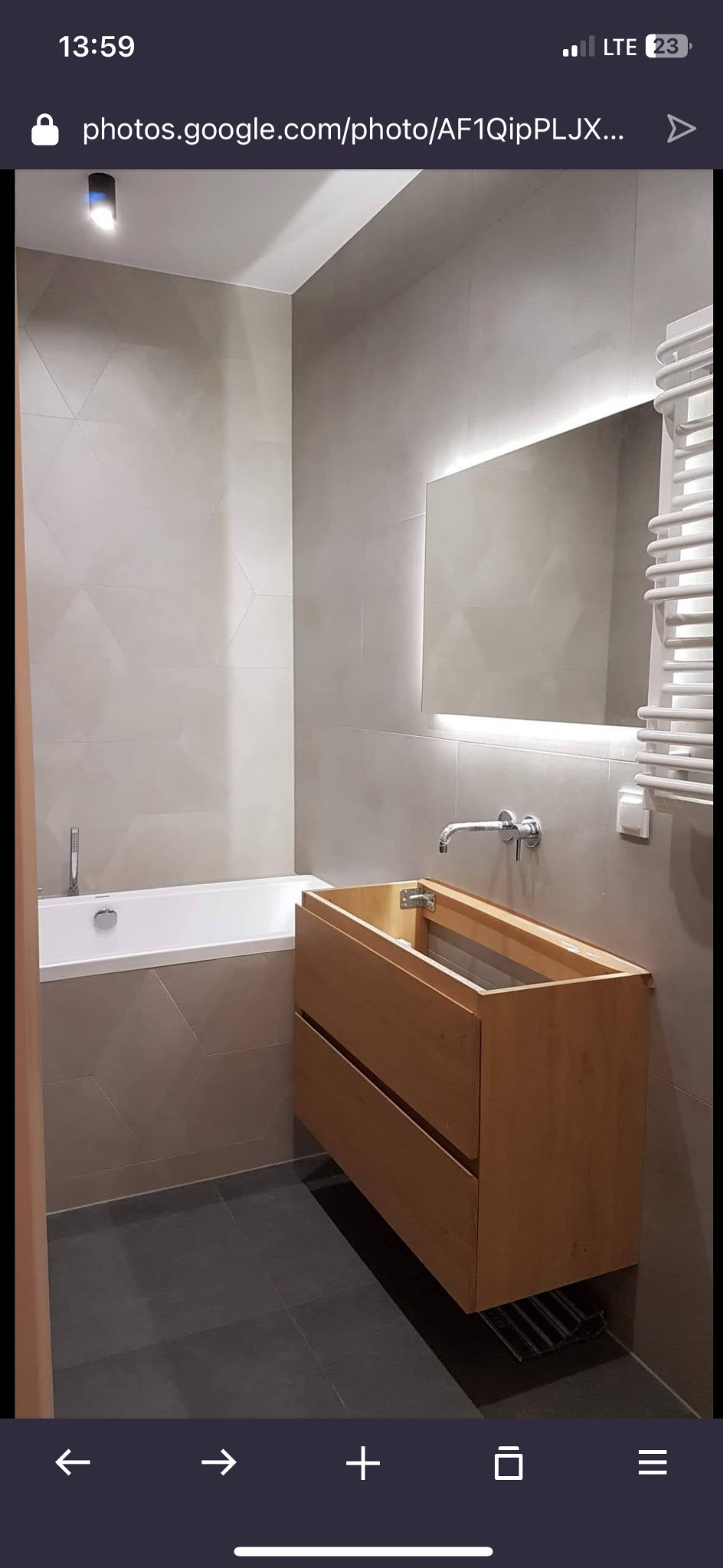 Nowoczesna łazienka z drewnianą szafką pod umywalkę bez blatu, podświetlanym lustrem i geometrycznymi płytkami na ścianach. Minimalistyczny design, ciepłe oświetlenie.