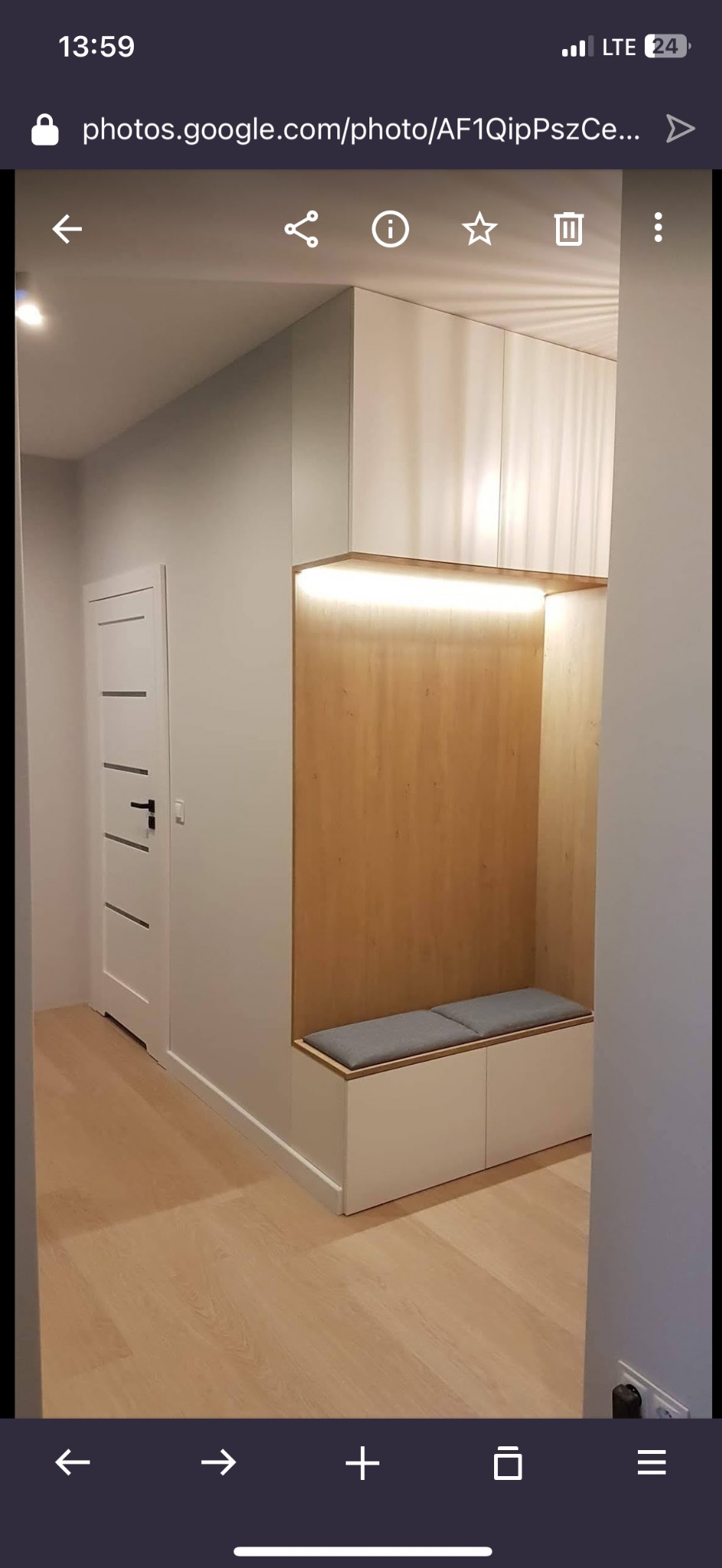 Nowoczesny przedpokój z zabudową meblową: białe szafki, drewniana wnęka z podświetleniem LED i siedziskiem. Minimalistyczny design, jasne kolory, drewniana podłoga.