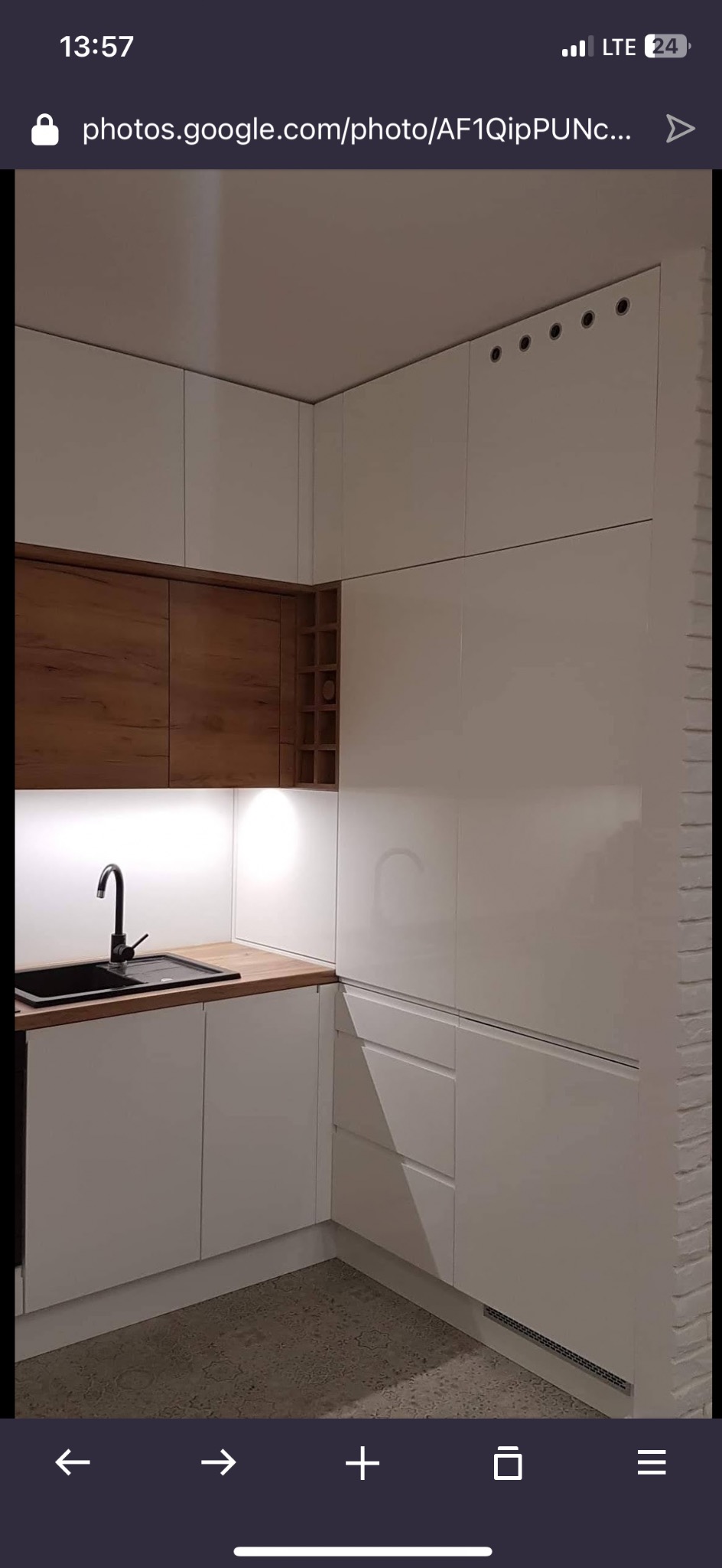 Nowoczesna kuchnia w bieli i drewnie: lakierowane fronty, drewniane szafki wiszące z półkami na wino, czarny zlew i bateria, oświetlenie LED podszafkowe.