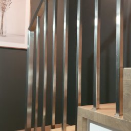 Norbert Turliński - Nowoczesne schody z drewnianymi stopniami i metalową balustradą, minimalistyczny design, jasne drewno, szare ściany, obraz w tle. Detal wykończenia wnętrza.