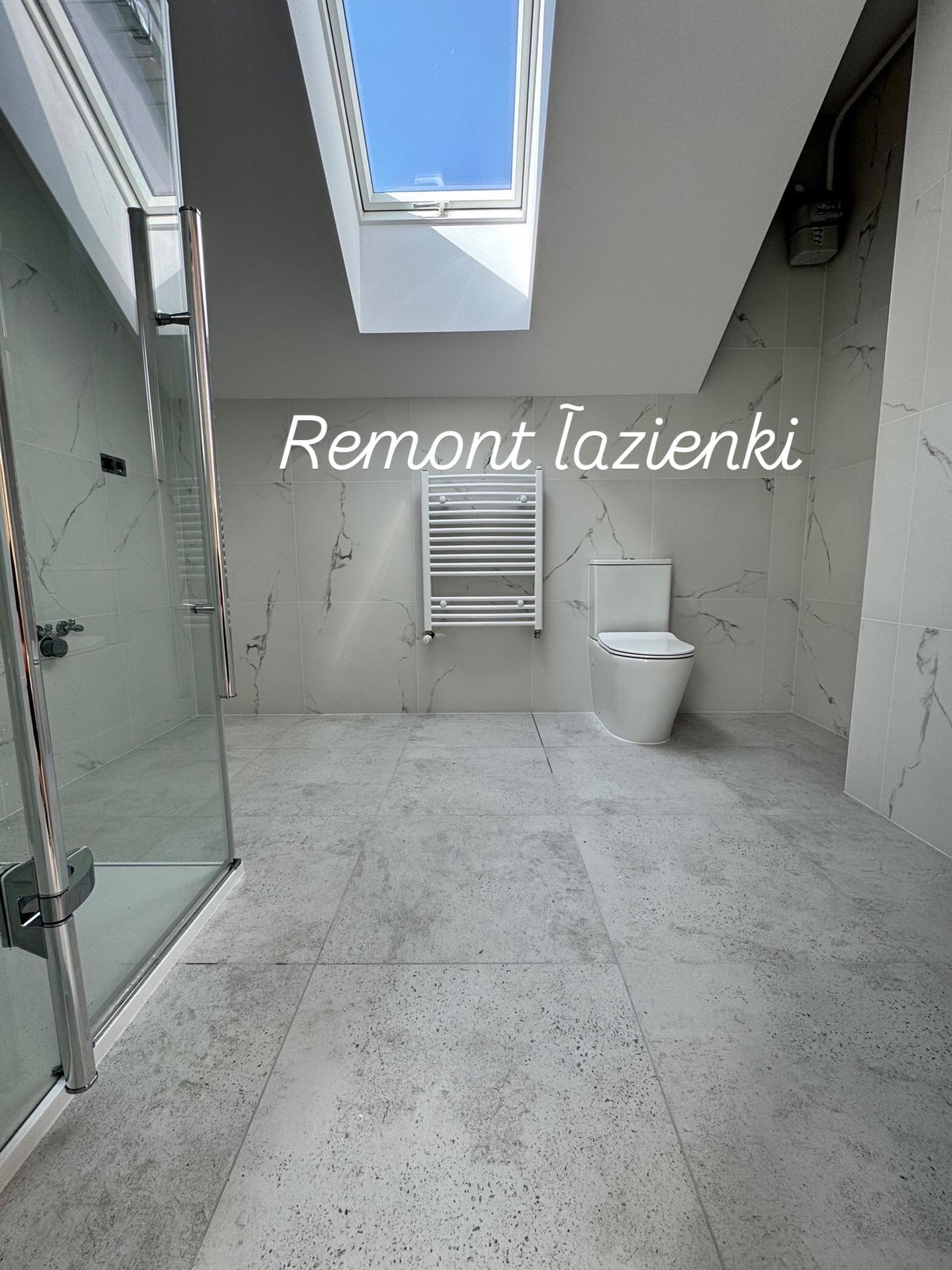 Jasna łazienka po remoncie z kabiną prysznicową, grzejnikiem drabinkowym i toaletą. Marmurowe płytki na ścianach i podłodze, okno dachowe wpuszcza naturalne światło.