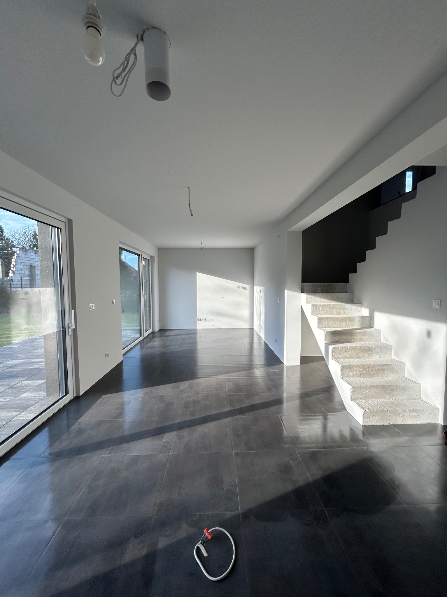 Przestronne wnętrze po remoncie: ciemna, błyszcząca podłoga, białe ściany, schody z surowego betonu. Widoczne niedokończone instalacje oświetleniowe.