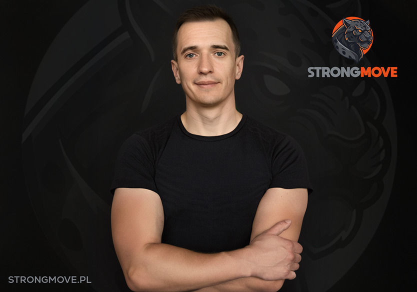 Portret mężczyzny w czarnej koszulce z logo StrongMove w tle. Uśmiechnięty, z założonymi rękami, prezentuje sylwetkę. Zdjęcie w ciemnej tonacji, z widocznym adresem strony.