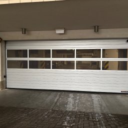 PM Tech Systemy Automatyki Bram Paweł Mirkowicz - Zamknięta, segmentowa brama garażowa Hormann z poziomymi panelami i przeszkleniami z siatki, zamontowana w garażu z ceglanymi ścianami i betonową posadzką.