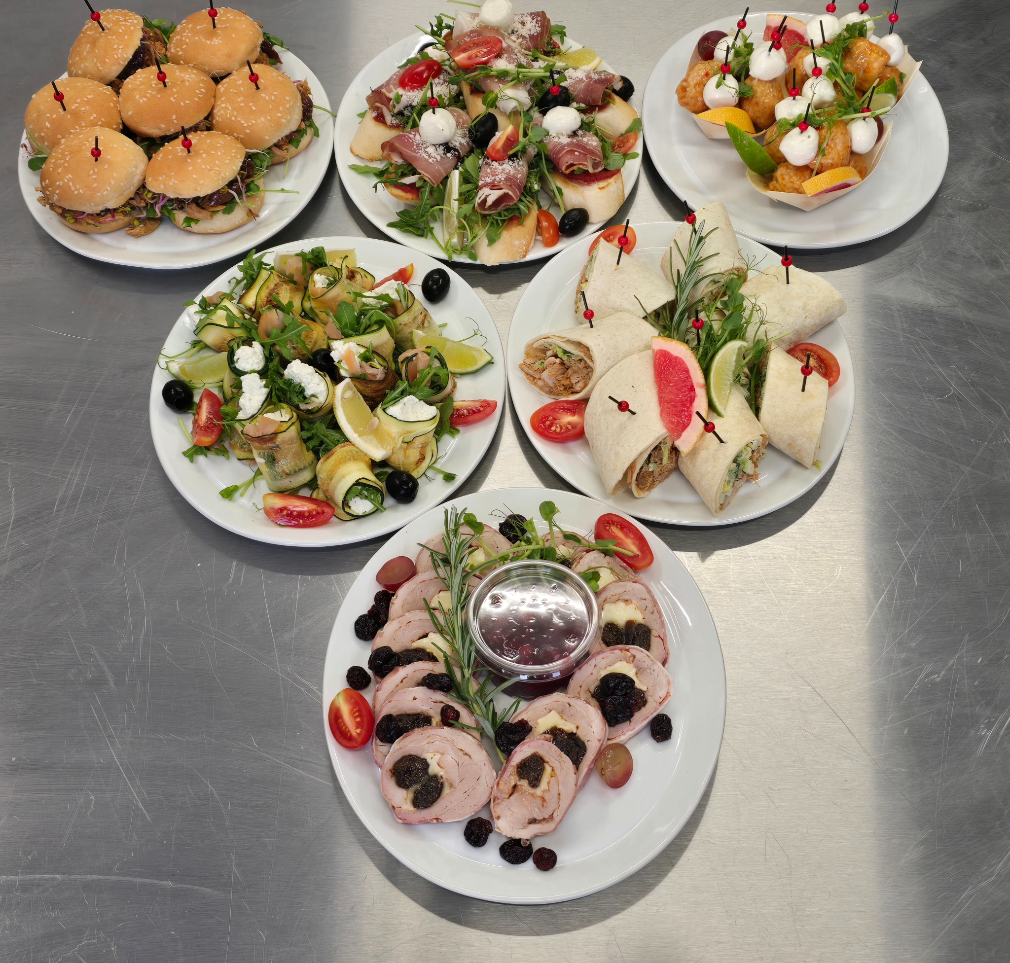 Elegancki zestaw cateringowy: mini burgery, roladki z cukinii, tortille i mięsne przekąski na białych talerzach, idealne na firmowe przyjęcie lub świąteczny stół.