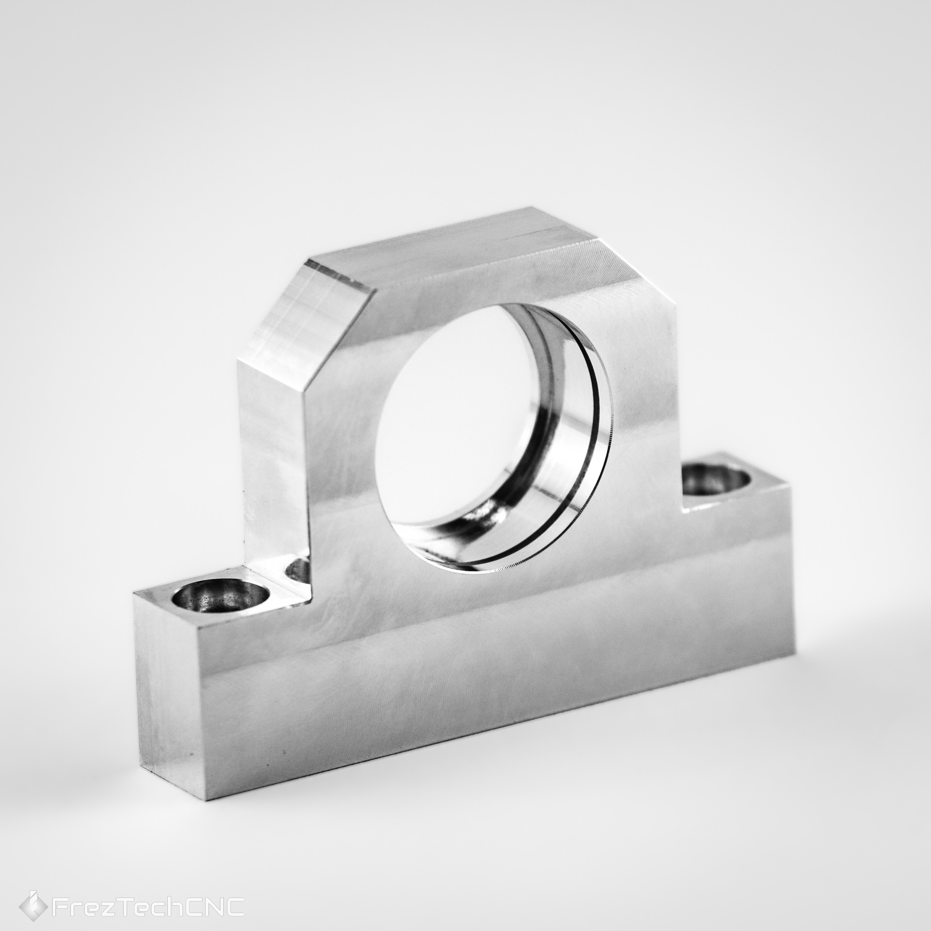 Precyzyjnie wykonany, srebrny element metalowy z otworem, obrobiony na maszynie. Widoczne ślady frezowania. Detal z dwoma otworami montażowymi.