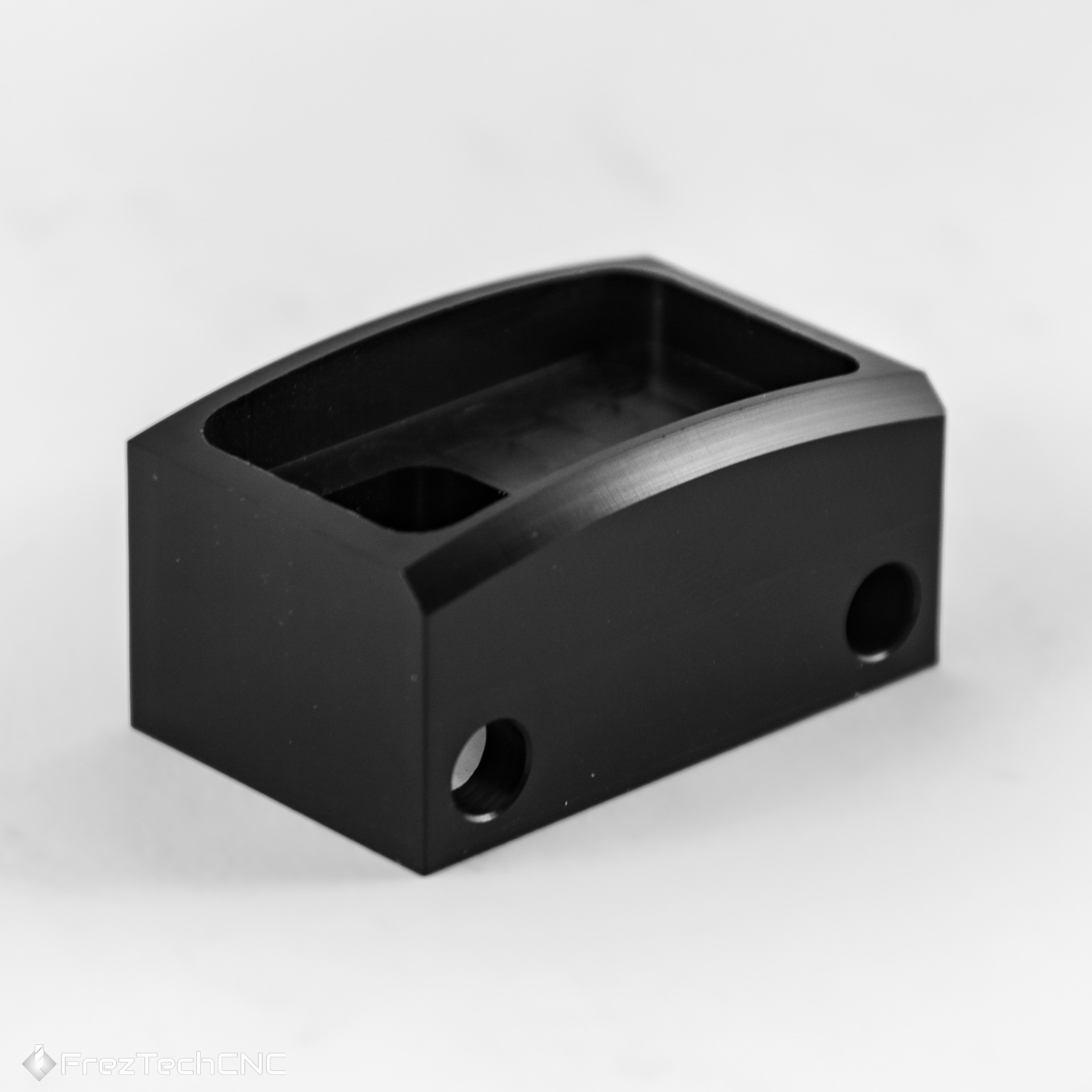 Czarny, precyzyjnie wykonany element z metalu z otworami, prawdopodobnie wykonany techniką skrawania, na jasnym tle. Widoczne detale i gładkie powierzchnie.