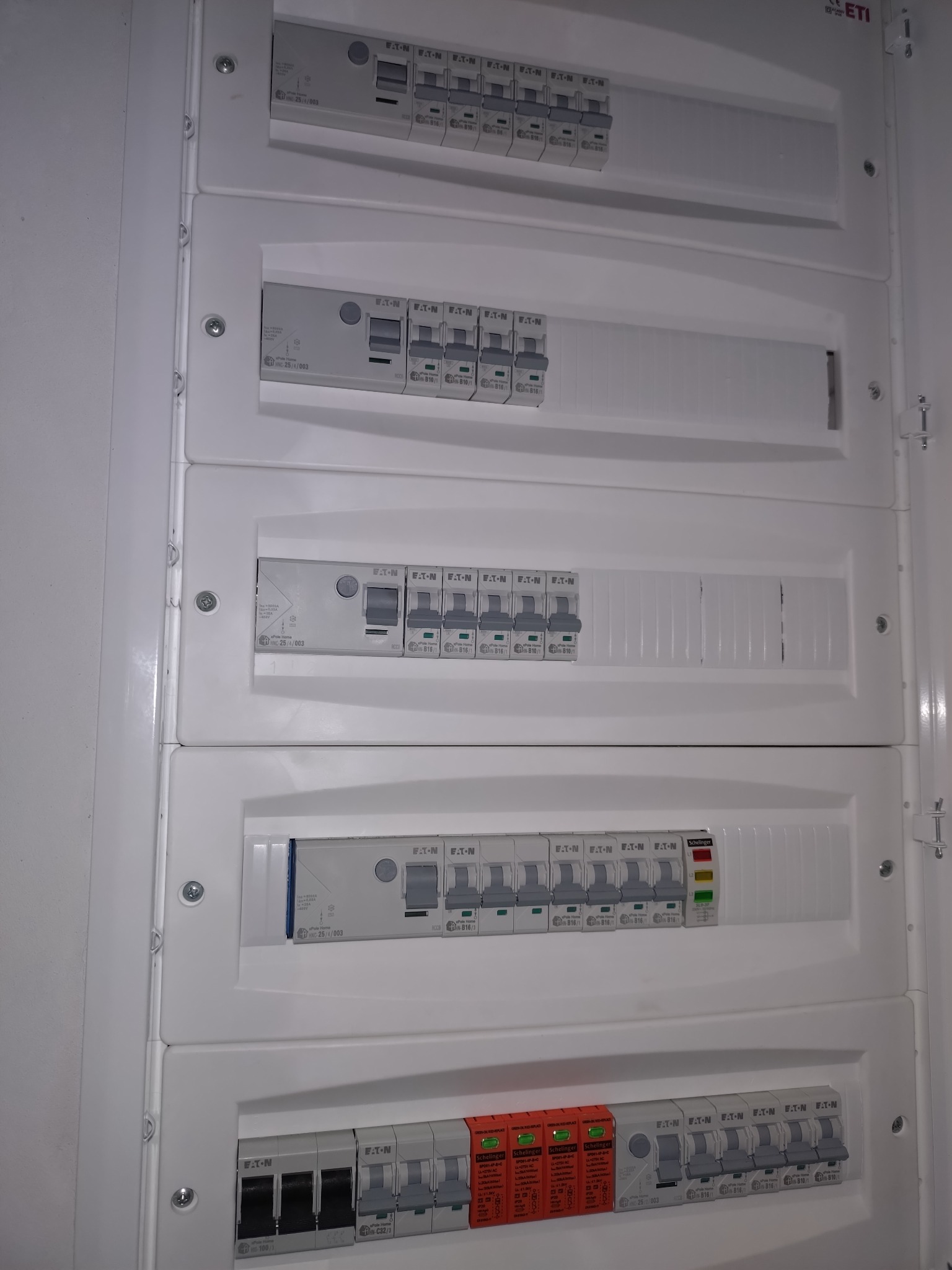 Rozdzielnica elektryczna z bezpiecznikami EATON i Schelinger, widok z bliska, prezentująca zainstalowane zabezpieczenia w białej obudowie.