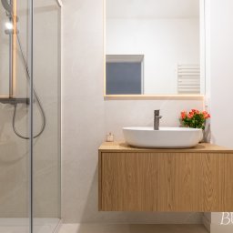 Bukabu Anna Pilch Projektowanie Wnętrz - Nowoczesna łazienka z kabiną prysznicową, umywalką nablatową na drewnianej szafce i podświetlanym lustrem. Minimalistyczny design z akcentem kolorystycznym w postaci kwiatów.