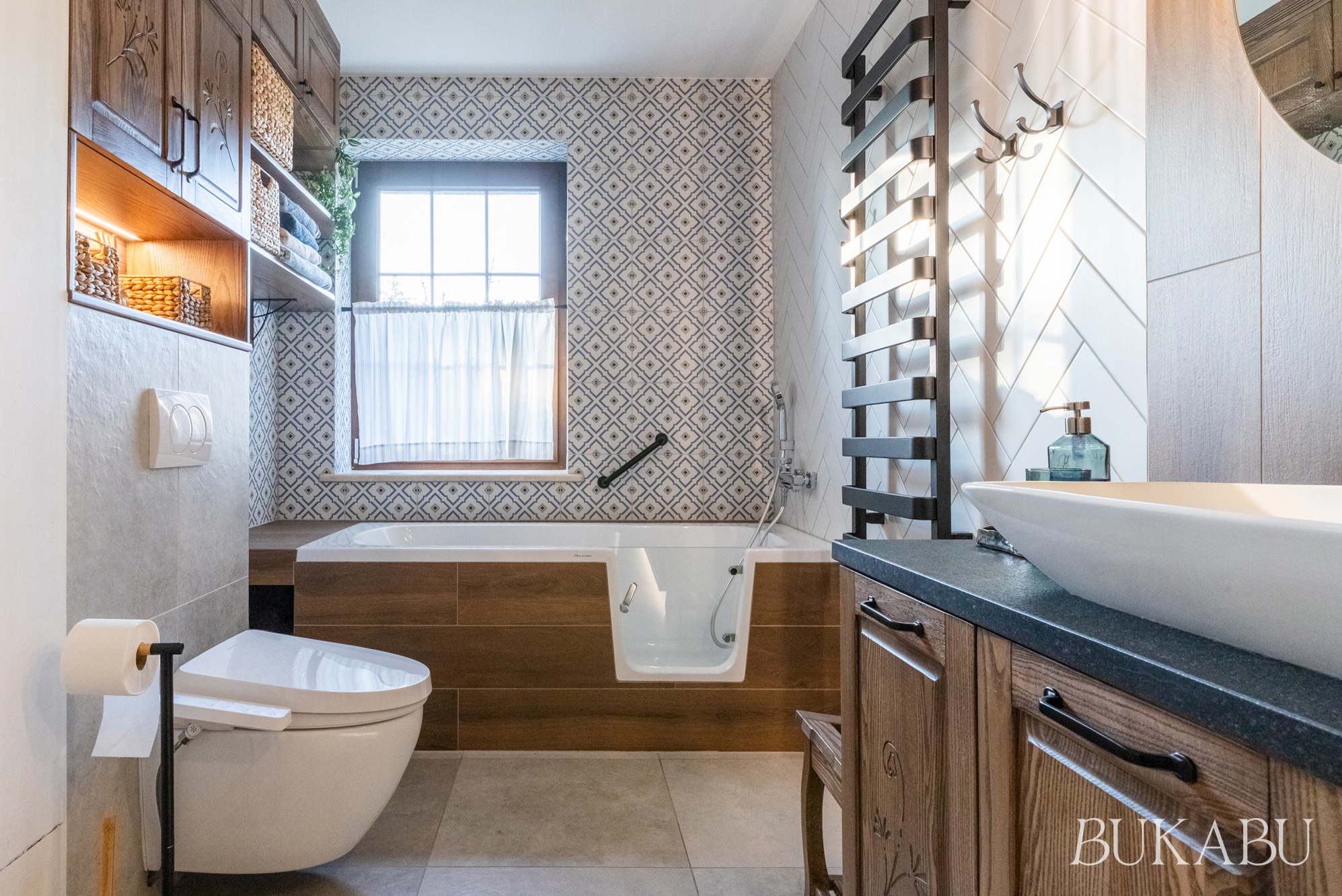 Funkcjonalna łazienka z wanną z drzwiczkami, umywalką nablatową i grzejnikiem drabinkowym. Użyto czterech rodzajów płytek i ciemnego drewna. Projekt uwzględnia potrzeby osób z niepełnosprawnością.