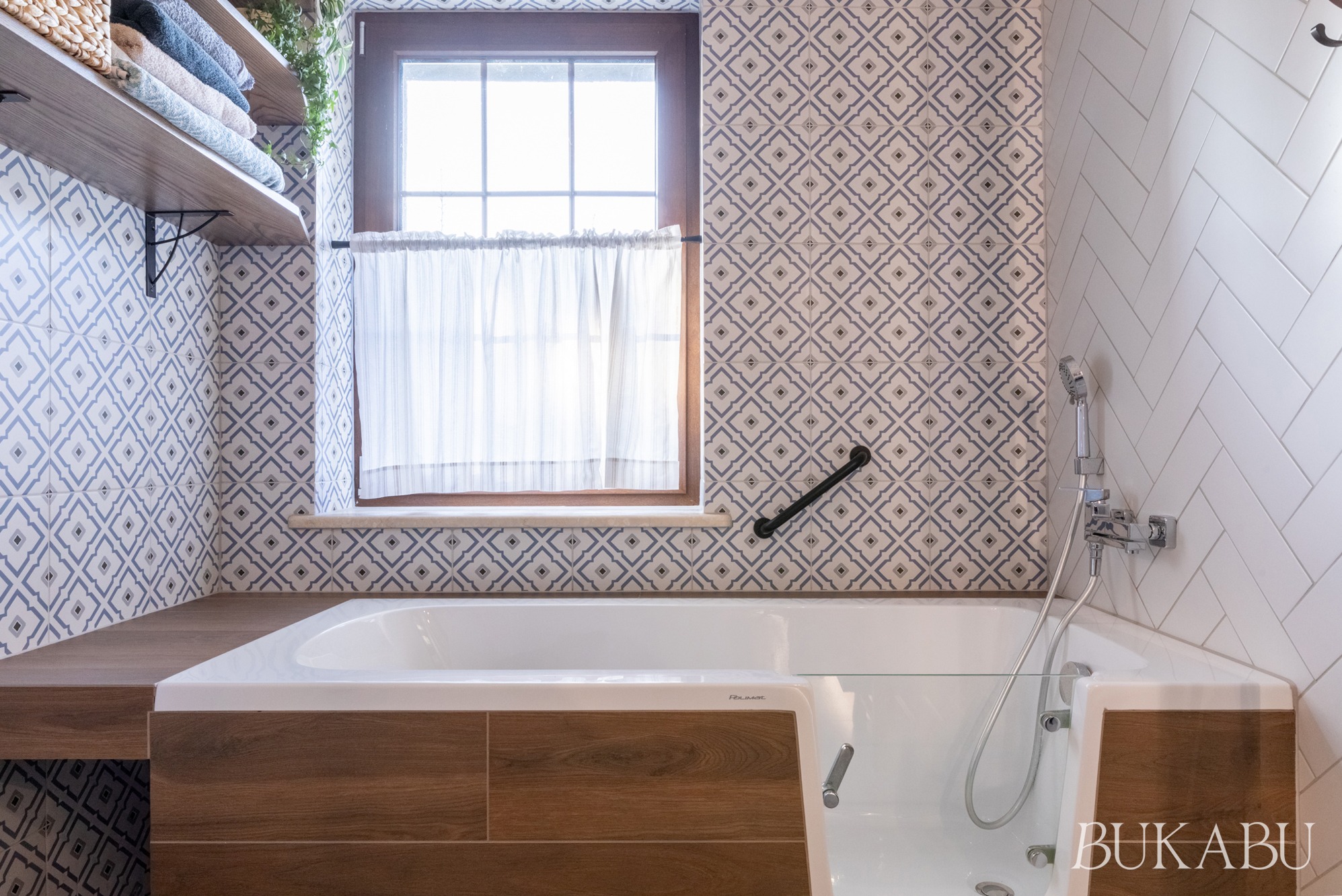 Funkcjonalna łazienka z wanną z drzwiczkami, drewnianymi akcentami i wzorzystymi płytkami. Udogodnienia dla osób z niepełnosprawnościami, naturalne światło.