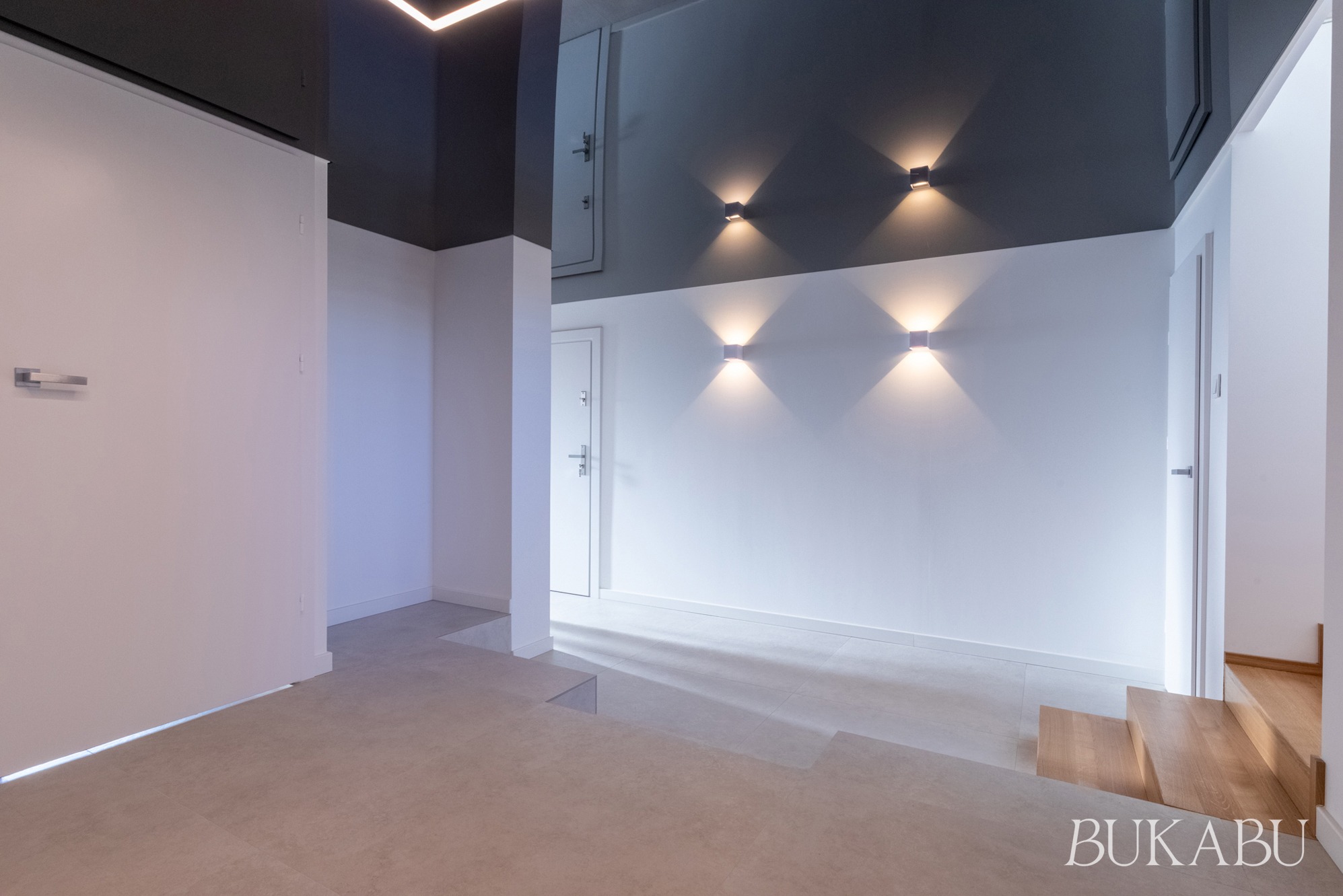 Nowoczesne wnętrze po metamorfozie: białe ściany, szary sufit z oświetleniem LED, drewniane schody. Minimalistyczny design z akcentami światła.