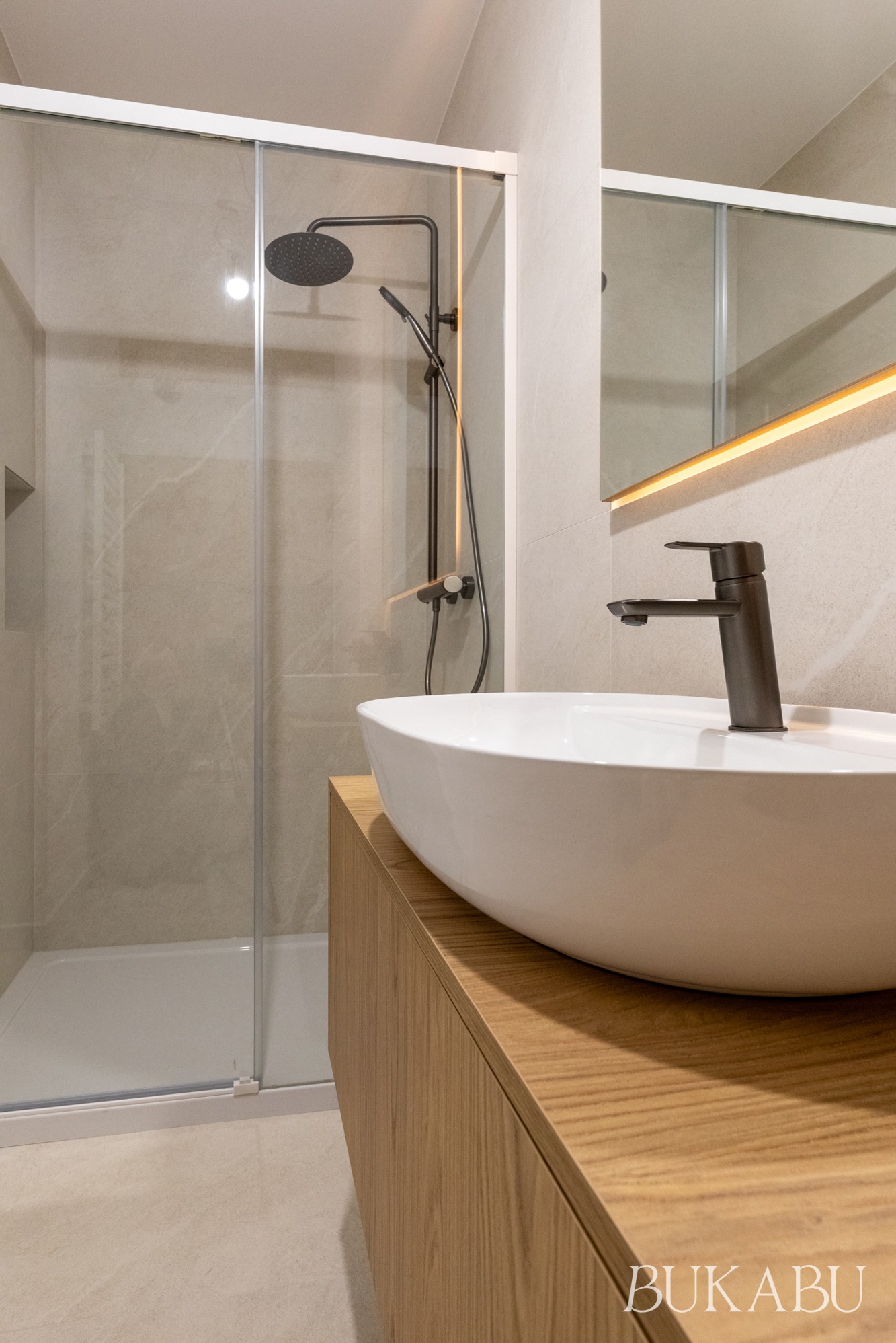 Nowoczesna łazienka z kabiną prysznicową typu walk-in, umywalką nablatową o owalnym kształcie i drewnianą szafką. Minimalistyczny design, stonowana kolorystyka.