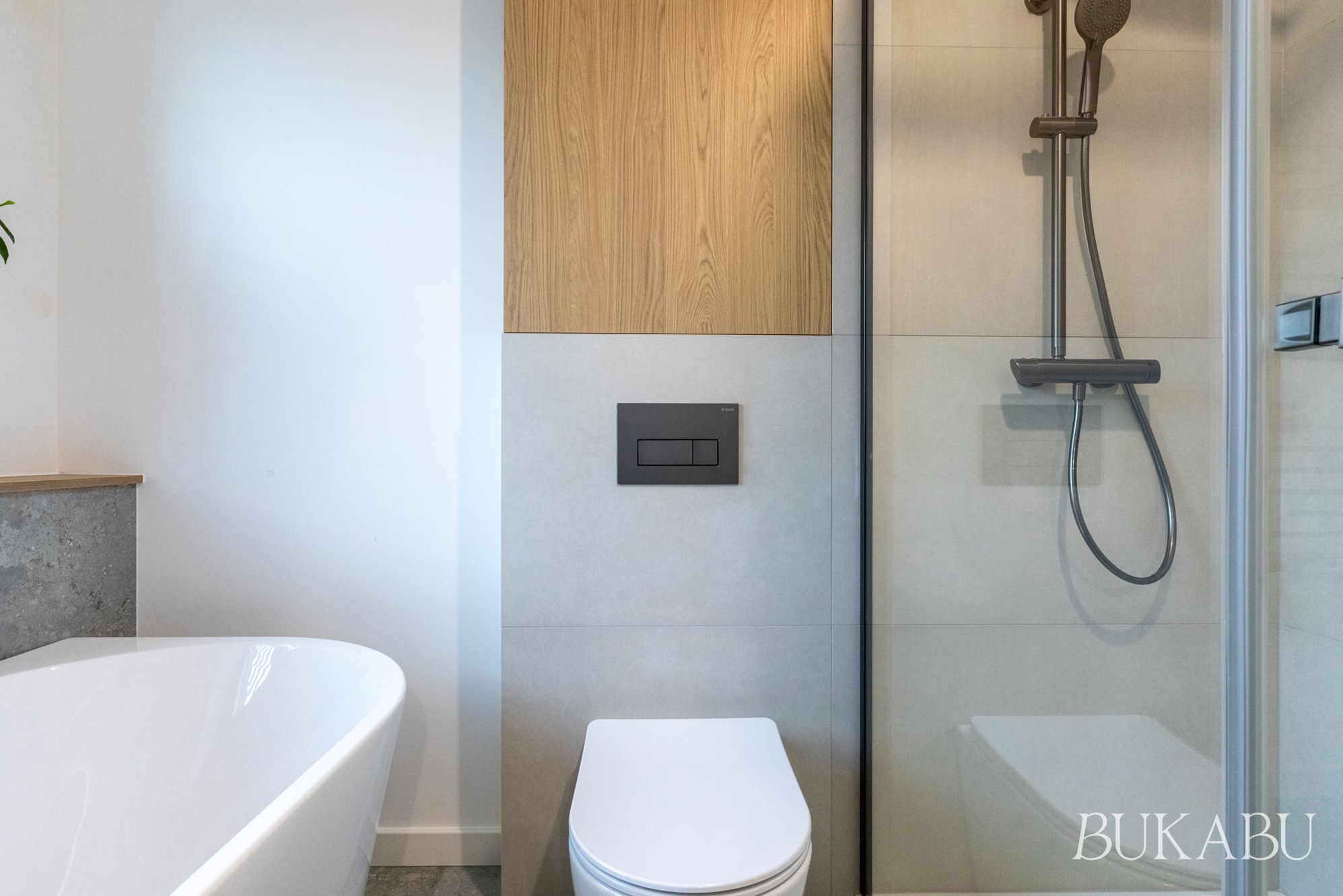 Nowoczesna łazienka z wolnostojącą wanną, kabiną prysznicową i drewnianym akcentem na ścianie. Minimalistyczny design, szaro-biała kolorystyka, eleganckie wykończenie.