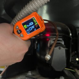 Technika Chłodnicza Jakub Mruk - Pomiar temperatury sprężarki chłodziarki za pomocą termometru laserowego. Widoczny przewód i elementy instalacji chłodniczej. Pomiar w trakcie serwisu.