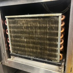 Technika Chłodnicza Jakub Mruk - Zanieczyszczony wymiennik ciepła w urządzeniu chłodniczym, widoczny wewnątrz metalowej obudowy. Usługa naprawy lodówek w Poznaniu.