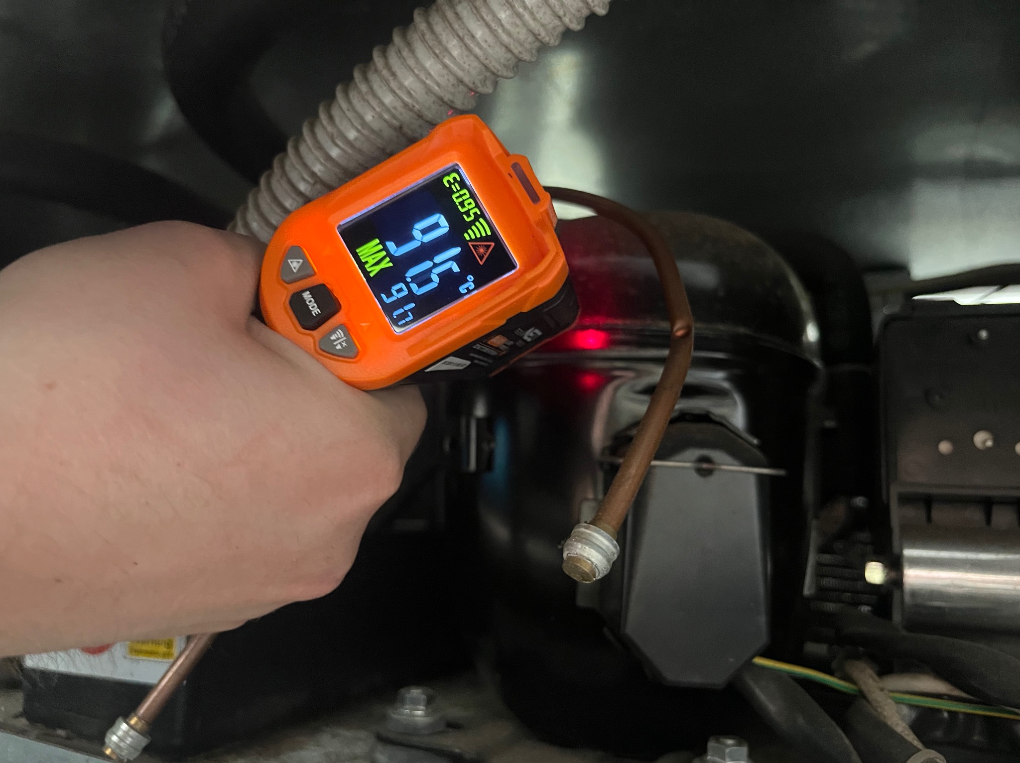 Pomiar temperatury sprężarki chłodziarki za pomocą termometru laserowego. Widoczny przewód i elementy instalacji chłodniczej. Pomiar w trakcie serwisu.