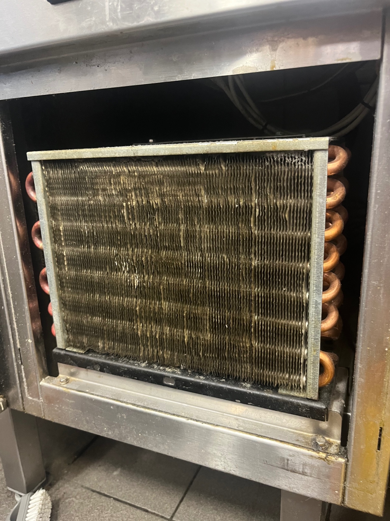 Zanieczyszczony wymiennik ciepła w urządzeniu chłodniczym, widoczny wewnątrz metalowej obudowy. Usługa naprawy lodówek w Poznaniu.