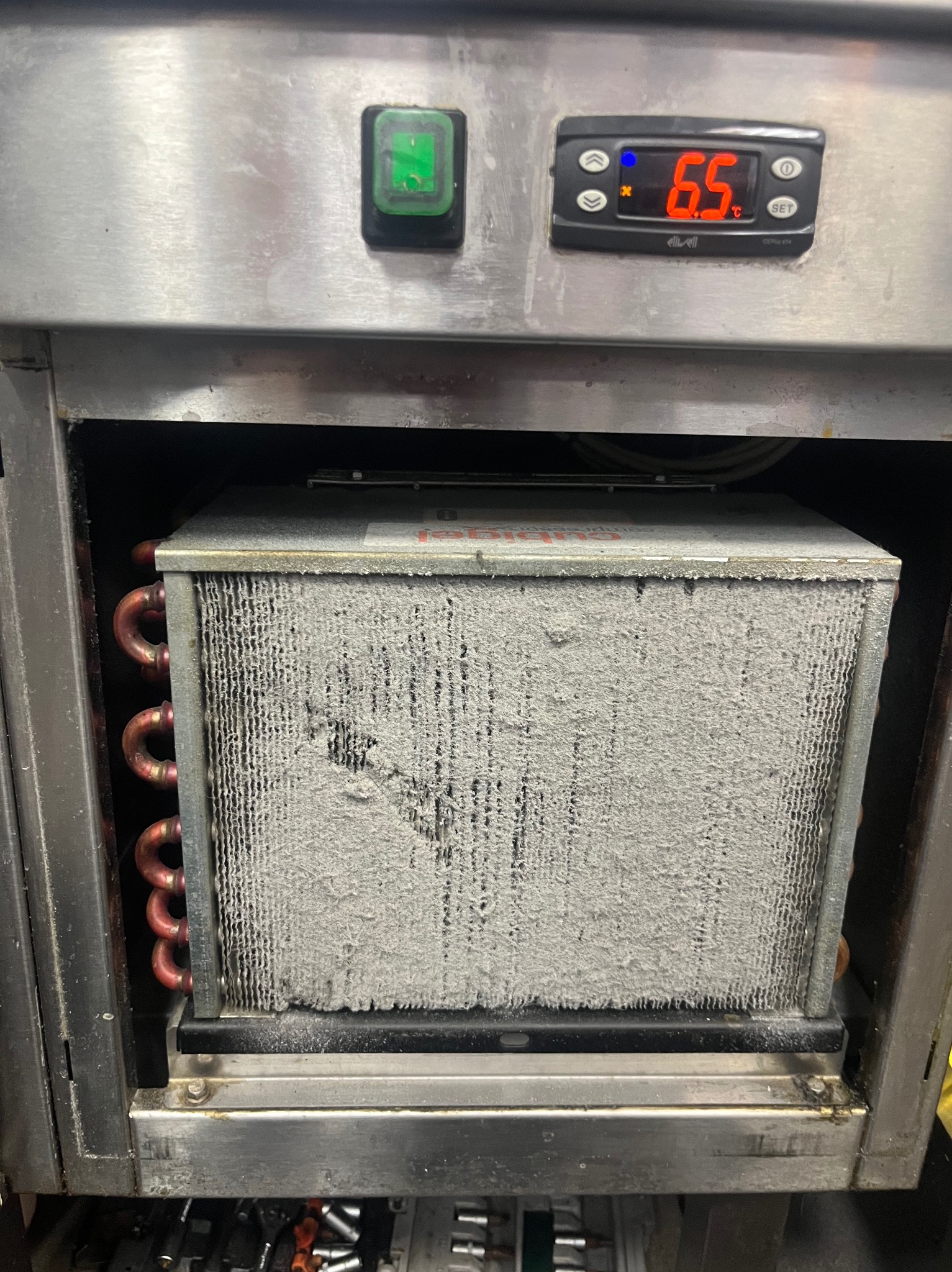 Zaszroniony parownik wewnątrz urządzenia chłodniczego, widoczne miedziane rurki i wyświetlacz temperatury wskazujący 6.5°C. Urządzenie w obudowie ze stali nierdzewnej.