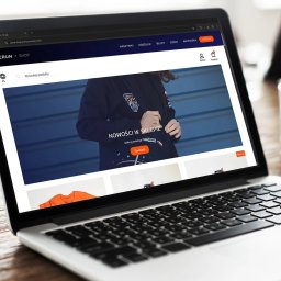 Pin Media Marcin Bąk - Laptop wyświetla stronę sklepu internetowego Perun z ofertą odzieży. Widoczny interfejs użytkownika, nawigacja i prezentacja produktów. Minimalistyczny design strony.