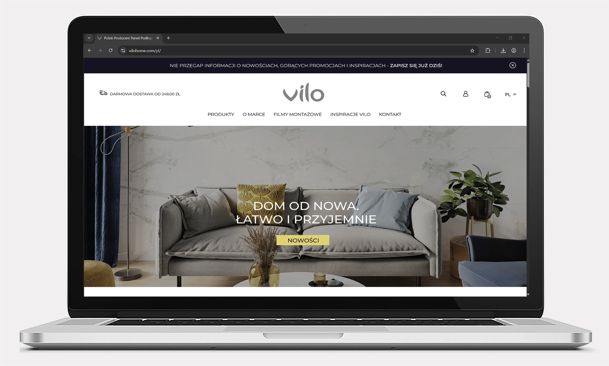 Laptop wyświetla stronę internetową Vilo z aranżacją wnętrza: szara sofa, marmurowe ściany i roślina. Widoczny pasek adresu z nazwą domeny vilohome.com/pl/.