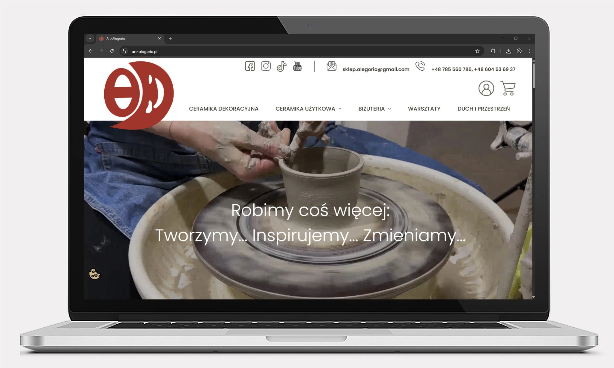 Laptop wyświetla stronę sklepu internetowego Art-Alegoria z ceramiką. Na ekranie widoczny film z warsztatu garncarskiego i menu z kategoriami produktów.