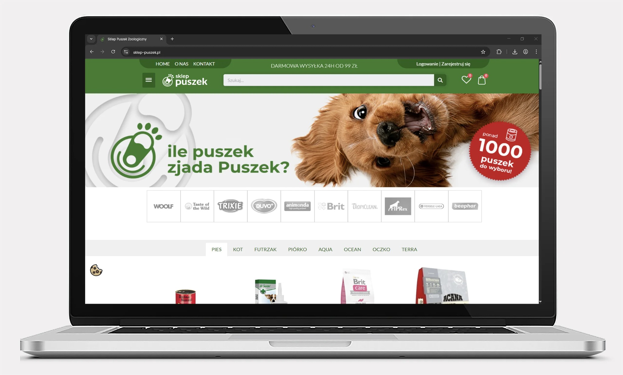 Laptop wyświetla stronę sklepu zoologicznego 'Sklep Puszek', z grafiką psa i hasłem 'Ile puszek zjada Puszek?'. Widoczne logo marek karm i akcesoriów dla zwierząt.