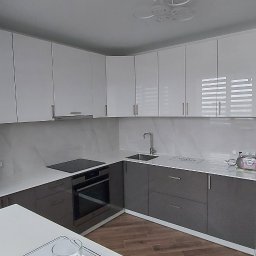 Novy Remont - Nowoczesna kuchnia w odcieniach bieli i szarości z błyszczącymi frontami, wyposażona w płytę indukcyjną i piekarnik. Widoczny czajnik elektryczny i radio w stylu retro.