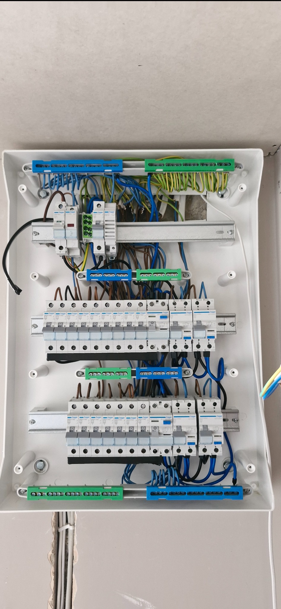 Rozdzielnica elektryczna z zainstalowanymi bezpiecznikami i przewodami w kolorach: niebieskim, zielonym, żółtym i brązowym. Widoczne szyny montażowe i elementy mocujące.
