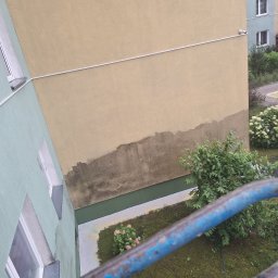 Kolor wash - Fragment elewacji budynku z widocznymi śladami wilgoci i zabrudzeń przed planowanym malowaniem. Widok z góry, z fragmentem niebieskiej barierki w kadrze.