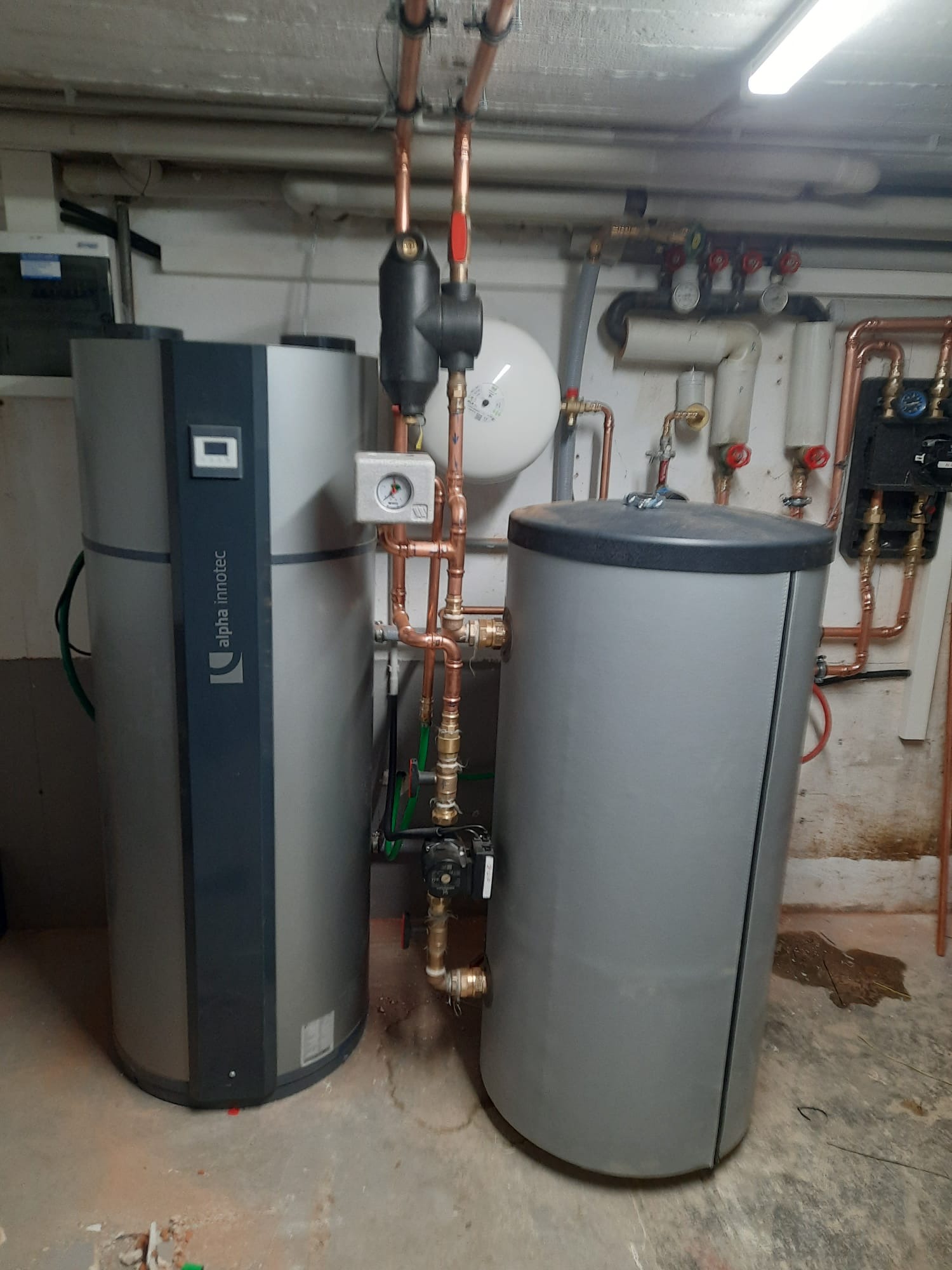Nowoczesna instalacja grzewcza z dwoma zbiornikami, rurami miedzianymi i zaworami w kotłowni. Jeden zbiornik marki Alpha Innotec.