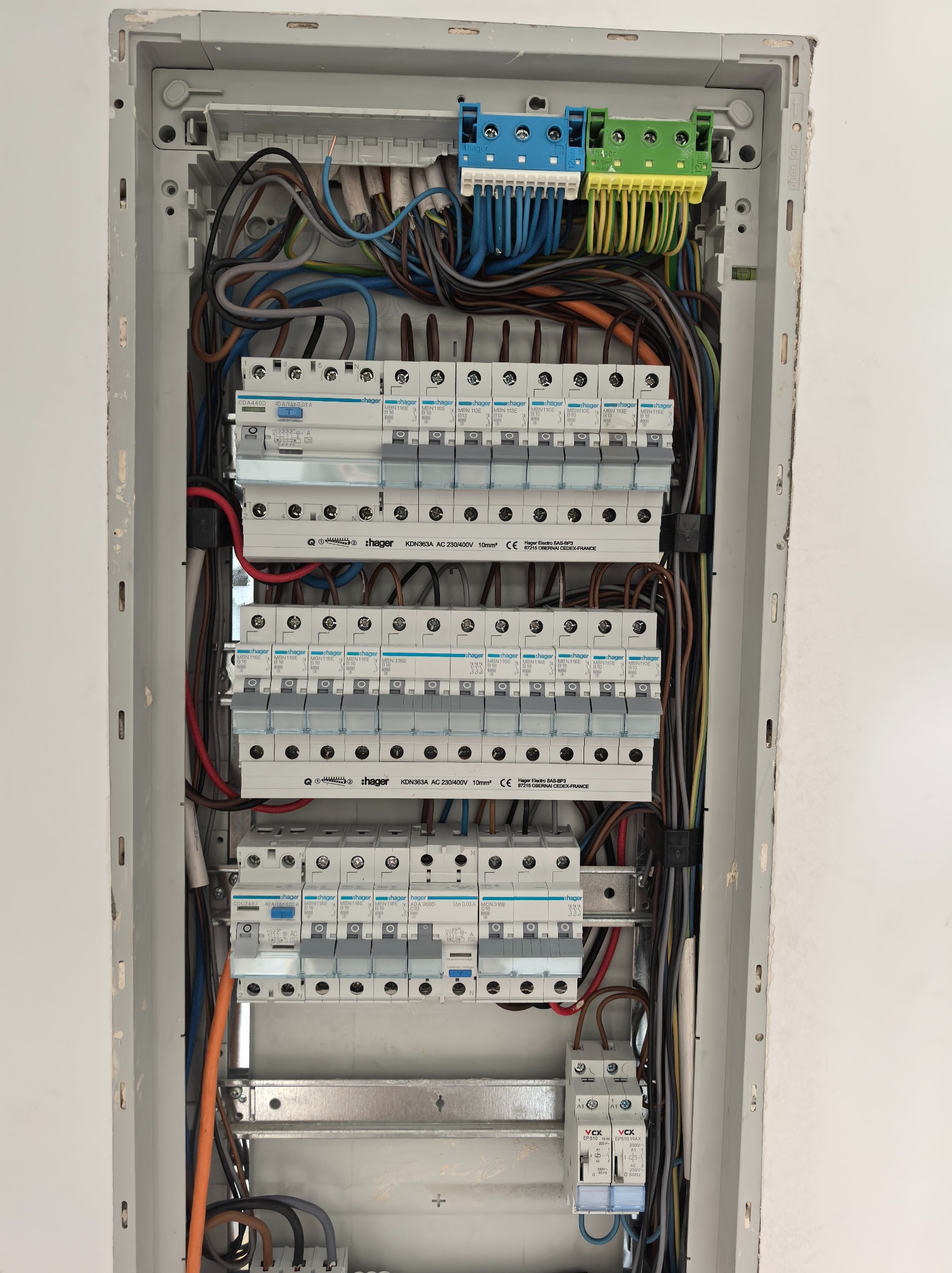 Rozdzielnia elektryczna Hager z zainstalowanymi bezpiecznikami i okablowaniem, widok z bliska na szarej ścianie. Element instalacji elektrycznej wewnątrz budynku.