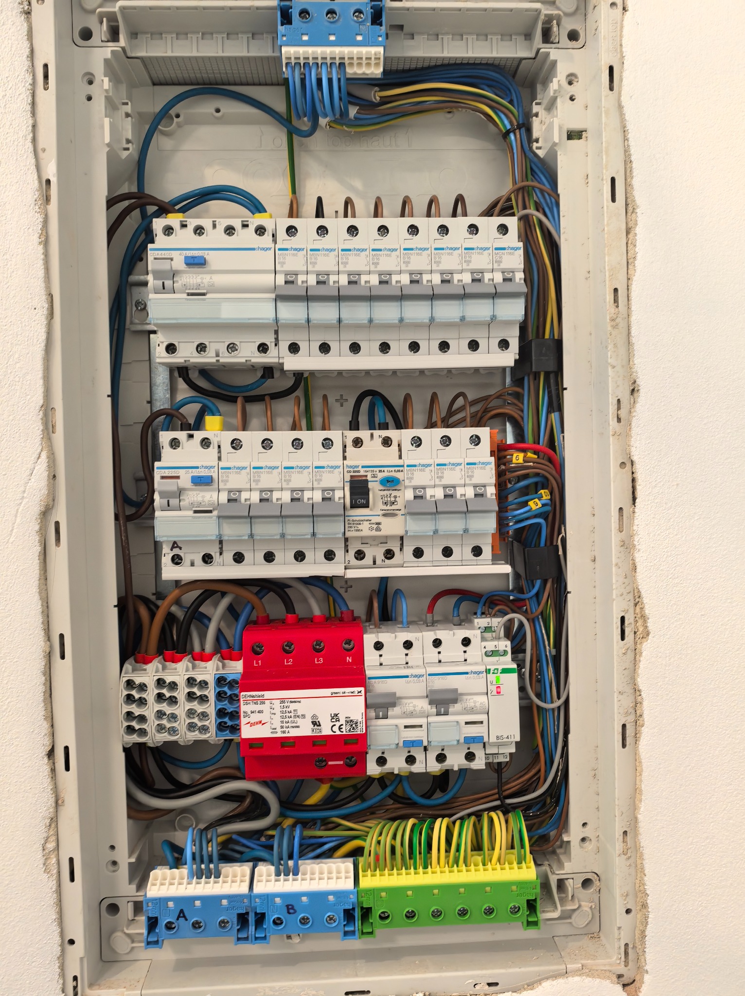 Rozdzielnica elektryczna Hager z zabezpieczeniami, widoczne bezpieczniki, przewody w różnych kolorach, zamontowana w białej obudowie w ścianie.