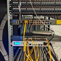 Pavel Skarynka - Panel krosowniczy z podłączonymi kablami Ethernet w serwerowni. Widoczne switche sieciowe, router i inne urządzenia rackowe. Żółte kable patchcord.