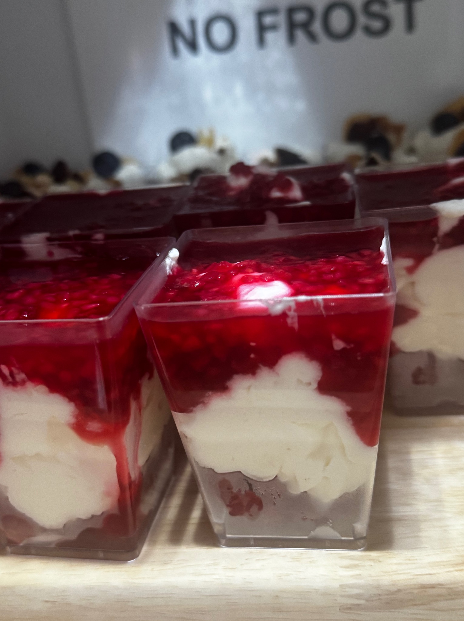 Deser w przezroczystych pojemnikach z czerwoną galaretką i kremem, ustawiony w rzędzie, z napisem 'NO FROST' w tle.
