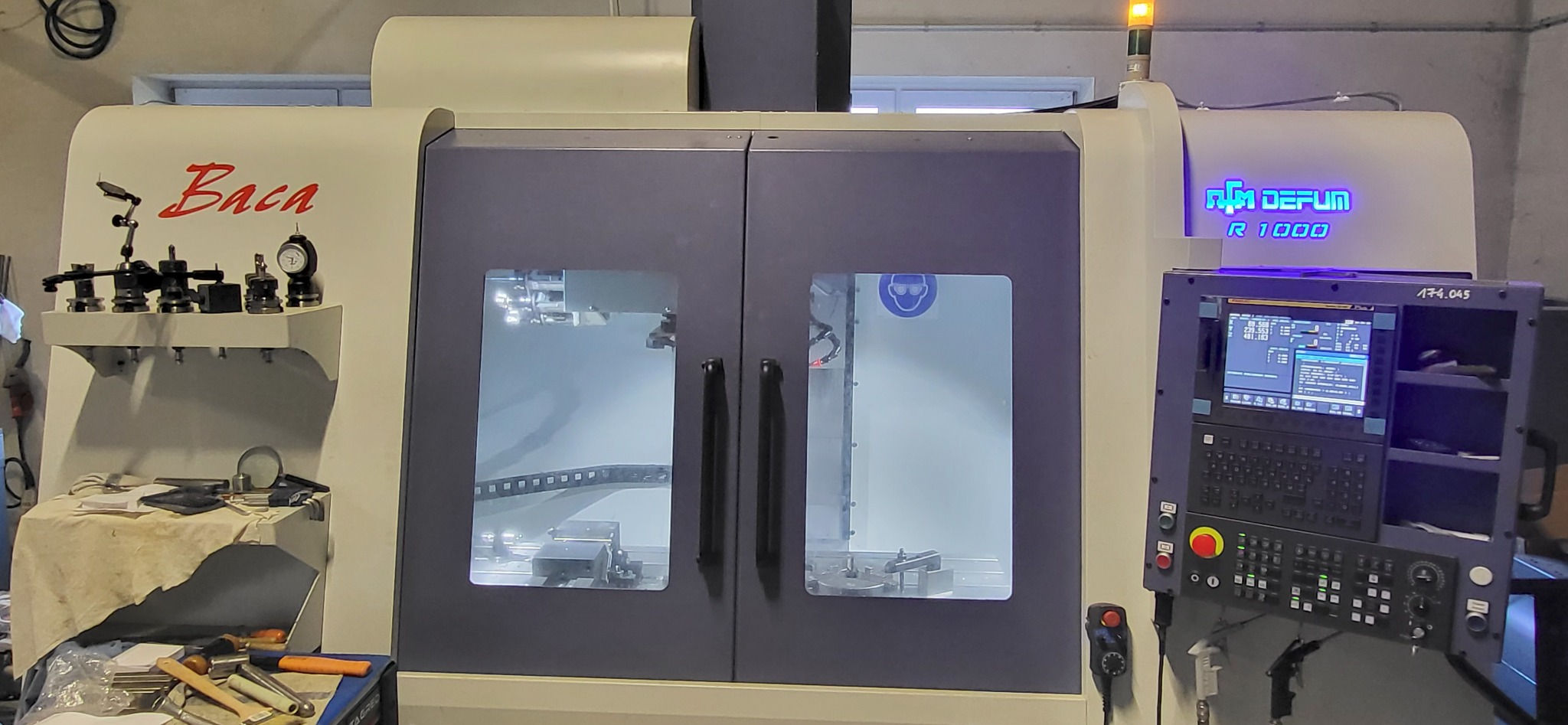 Nowoczesna frezarka CNC marki Baca Defum R1000 z widocznym panelem sterowania i narzędziami, gotowa do precyzyjnej obróbki metalu w warsztacie.