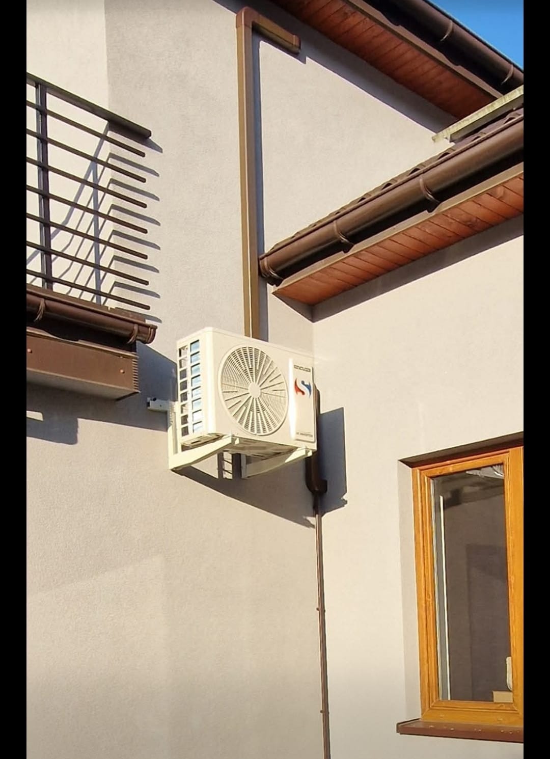 Biała jednostka zewnętrzna klimatyzacji zamontowana na elewacji budynku w Knurowie. Widoczne rury odprowadzające skropliny i elementy instalacji.