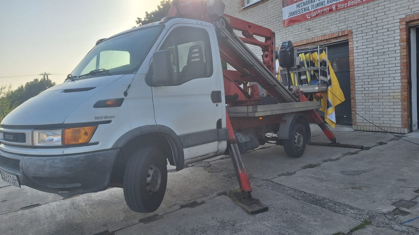 Laweta Iveco z podnośnikiem Sorage na tle warsztatu. Widoczny napis: Mechanika, tłumiki, zawieszenia. Stare Bielice. Usługi motoryzacyjne.