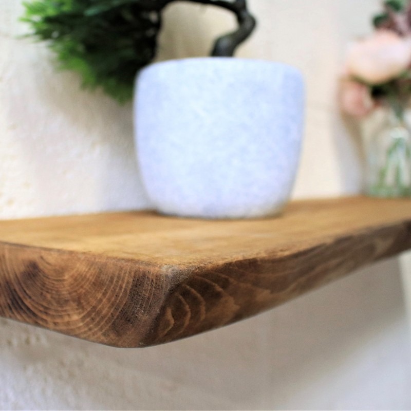 Rustykalna, drewniana półka ścienna z widocznym usłojeniem, na której stoi biała doniczka z rośliną. Ujęcie z bliska, podkreślające naturalny charakter drewna.