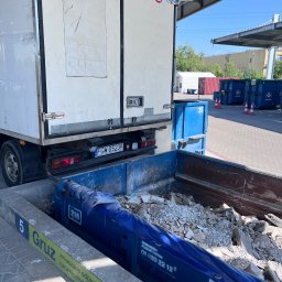 Twoja Przeprowadzka-Transport - Ciężarówka z otwartymi drzwiami załadunkowymi, tyłem do kontenera wypełnionego gruzem i odpadami budowlanymi na terenie punktu recyklingu.
