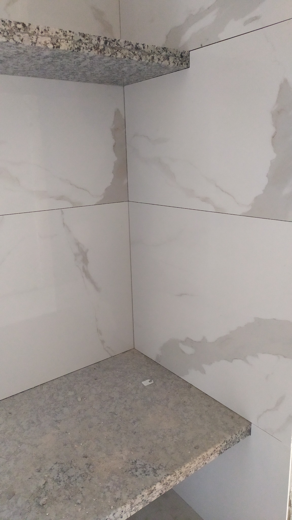 Wykończona wnęka z białych płytek imitujących marmur i szarego blatu z granitu. Widoczne precyzyjne fugi i dopasowanie elementów. Minimalistyczny design.